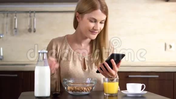 美丽的年轻迷人的女人早餐吃玉米片并使用她的智能手机视频的预览图