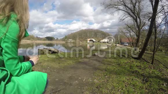 穿绿色外套的金发女人在湖边喂鸭子4K视频的预览图
