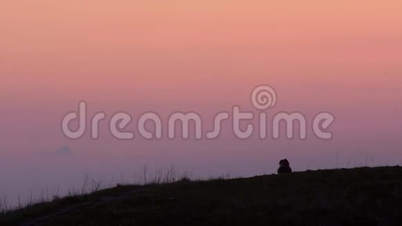 日落时分在山上看智能手机的年轻女性剪影视频的预览图