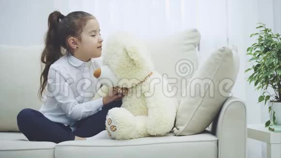 快乐的小女孩坐在沙发上抱着一个大泰迪熊视频的预览图