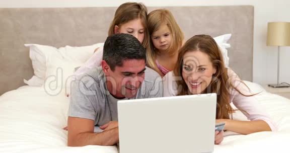 父母和女儿躺在床上用笔记本电脑上网购物视频的预览图