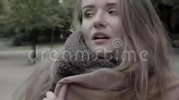 在寒冷的秋日里一个漂亮体贴的女人坐在公园的长凳上视频的预览图