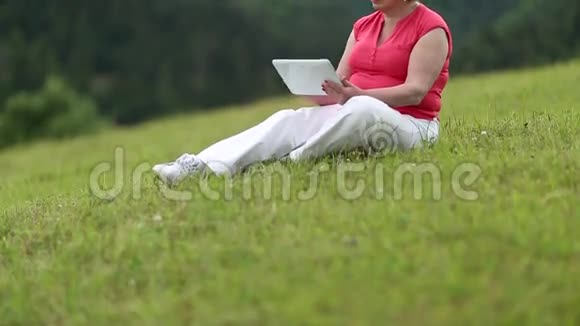 女人坐在绿草上用平板电脑视频的预览图