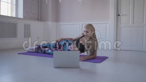 家庭健身年轻女子在训练伸展肌肉和关节在网上观看笔记本电脑上的视频视频的预览图