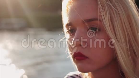美丽的年轻白种人女孩金发和红唇在日落前的水肖像特写镜头视频的预览图