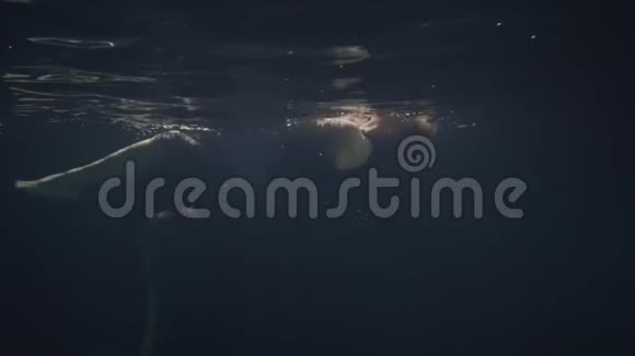 穿着黑色裙子在黑暗背景下水下游泳的时装模特视频的预览图