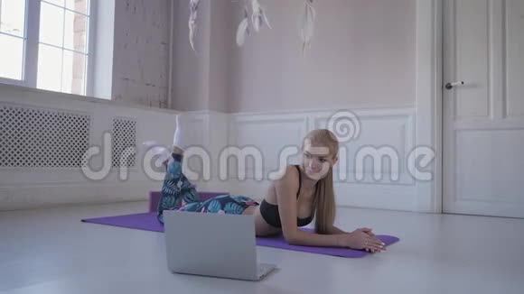 家庭健身年轻女子在训练伸展肌肉和关节在网上观看笔记本电脑上的视频视频的预览图