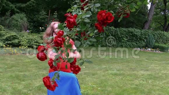孕妇在美丽的玫瑰丛边坐在公园里打电话视频的预览图