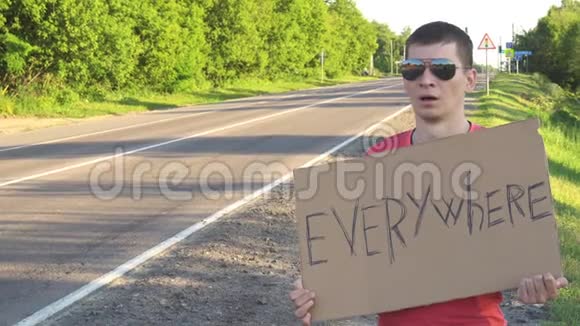 徒步旅行的年轻成年男子到处都在州际公路上举着一个大拇指的标牌视频的预览图