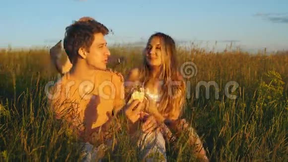 快乐的一对夫妇坐在田野里看日落视频的预览图
