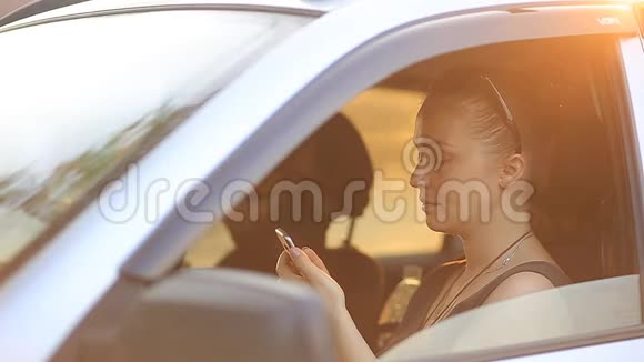 日落时分戴着墨镜红发的年轻美女坐在车轮后面手里拿着手机视频的预览图