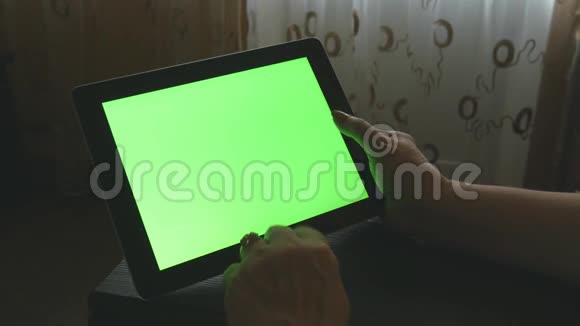 一位老年妇女坐在家里的沙发上使用带有绿色屏幕的数字平板电脑视频的预览图