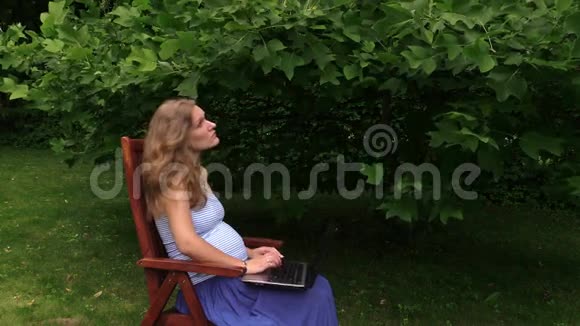 孕妇在郁金香树下的椅子上用电脑工作视频的预览图