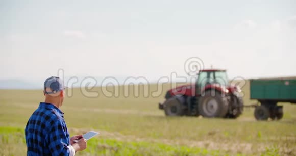农民在农场看拖拉机时使用数字平板电脑视频的预览图