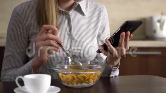 美丽的年轻迷人的女商人早餐吃玉米片并使用她的智能手机视频的预览图