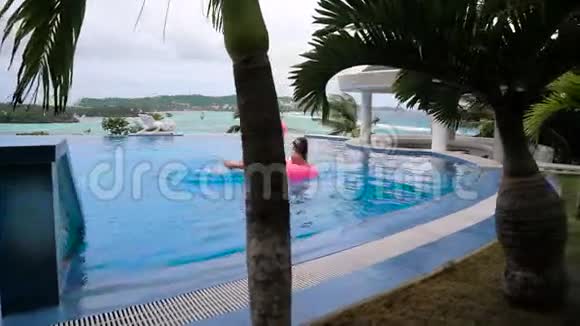 美丽的年轻女子喝着椰子在游泳池的粉红色充气床垫上放松漂亮的模特视频的预览图
