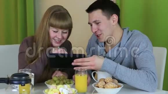 年轻快乐的一对相爱的夫妇看着平板电脑在早餐时交谈视频的预览图