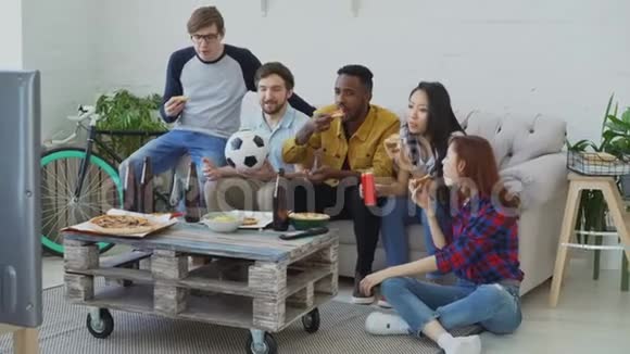 快乐的朋友体育迷们一起看电视上的足球锦标赛一起在家吃披萨喝啤酒视频的预览图