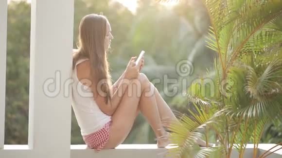 女人使用智能手机坐在露台上背景是花园视频的预览图