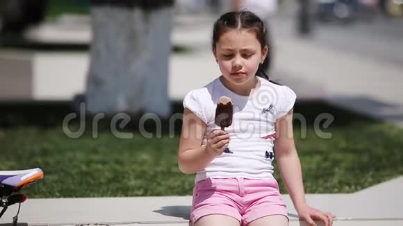 可爱的小女孩在阳光明媚的夏日在城市公园吃冰淇淋视频的预览图