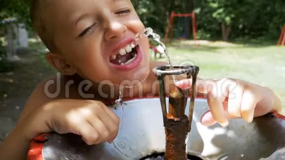 快乐的男孩有趣的饮用水从一个饮用喷泉在游乐场慢动作视频的预览图