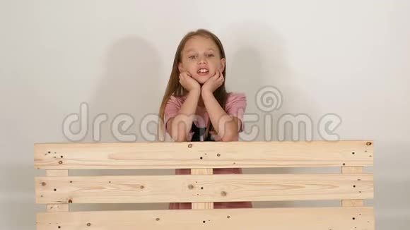 白色背景的工作室里靠近长凳的可爱小女孩的肖像视频的预览图