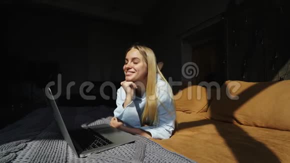 用手提电脑躺在床上微笑迷人的女人视频的预览图