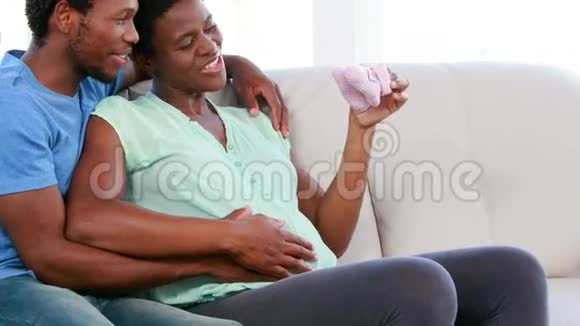 在沙发上展示婴儿鞋的孕妇视频的预览图