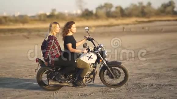 美丽的年轻女子摩托车手和他的女朋友骑摩托车在沙漠日落或日出两个女人骑自行车视频的预览图