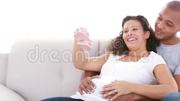在沙发上展示婴儿鞋的孕妇视频的预览图