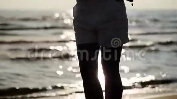 穿白色短裤的女孩在海滩上摆姿势背景上的海浪夏日日落视频的预览图