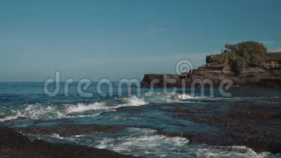 蓝色的平静的水小海浪在黑暗的岩石上洗涤和飞溅视频的预览图