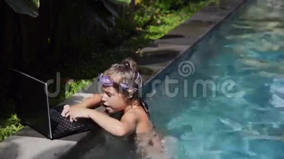 快乐的小女孩在游泳池里用笔记本电脑视频的预览图