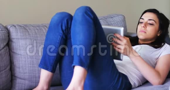 漂亮的女士在沙发上放松时使用数码平板电脑视频的预览图