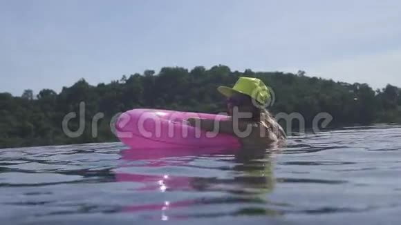 漂亮的年轻女人穿着比基尼黄色的帽子和紫色的太阳镜带着粉红色的充气戒指在无限的屋顶游泳池里游泳视频的预览图