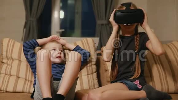 哥哥和姐姐在家坐在沙发上玩游戏用虚拟现实眼镜幸福家庭视频的预览图
