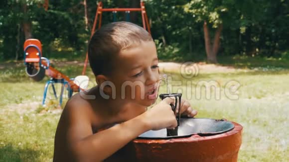 快乐的男孩有趣的饮用水从一个饮用喷泉在游乐场慢动作视频的预览图