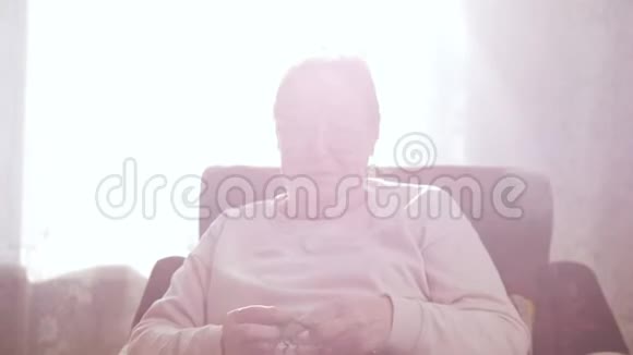 一位老妇人喜欢坐在扶手椅上在窗户的背景上编织视频的预览图