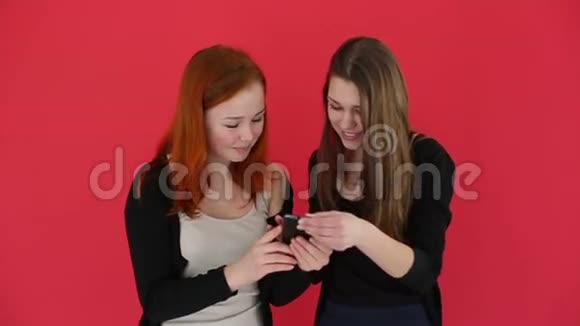 女孩用智能手机拍摄自我肖像看照片微笑和笑慢动作红工作室背景视频的预览图