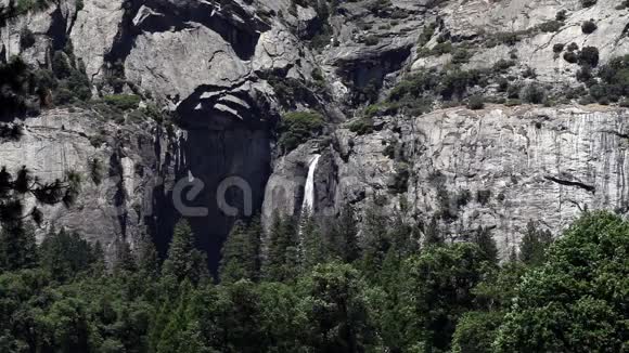 从远处的岩石和树木下约塞米蒂瀑布视频的预览图