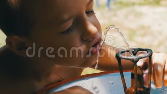 快乐的小男孩滑稽地从游乐场的饮水喷泉中喝水慢动作视频的预览图