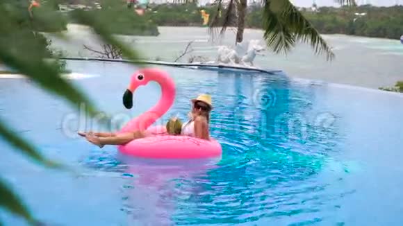 美丽的年轻女子喝着椰子在游泳池的粉红色充气床垫上放松漂亮的模特视频的预览图
