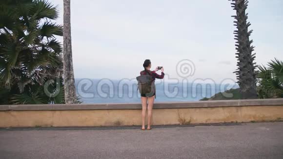 女旅行者欣赏海景用智能手机在海滩上拍照视频的预览图