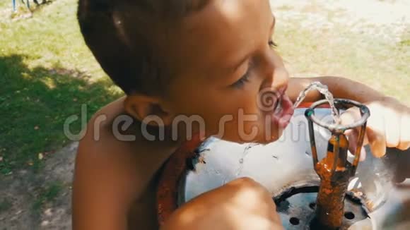 快乐的小男孩滑稽地从游乐场的饮水喷泉中喝水慢动作视频的预览图