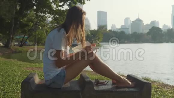 年轻女子坐在公园的长凳上写日记视频的预览图