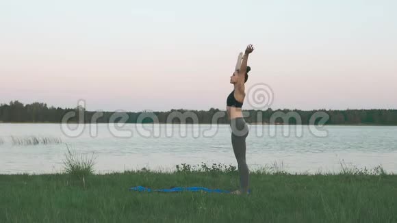 美丽的年轻女子在日出时在蓝色的瑜伽垫上做瑜伽安静的风景视频的预览图