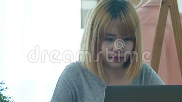 美丽的年轻微笑的亚洲女人在家工作时在笔记本电脑上工作视频的预览图