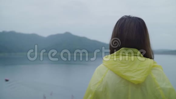 慢动作年轻的亚洲女人在湖边穿着雨衣玩雨时感到快乐视频的预览图