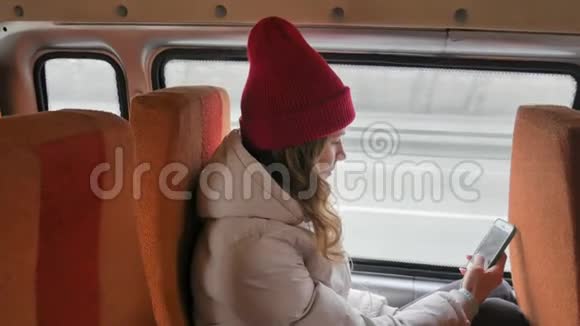 年轻开朗的女人戴着红帽子在一个悲伤的日子乘公共汽车旅行她在智能手机上拍照视频的预览图