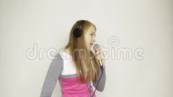 年轻女孩听着耳机里的音乐拿着麦克风唱歌和有趣的舞蹈视频的预览图